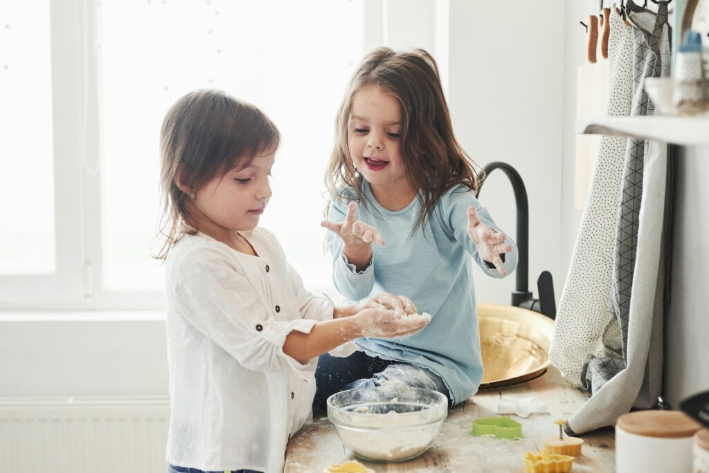 Children's games. Preschool friends learning how to cook with flour in the white kitchen