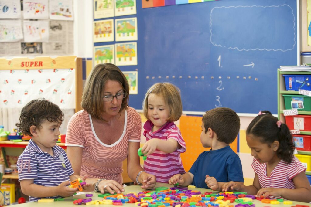 Female teacher with preschool boys and girls learning alphabet in classroom