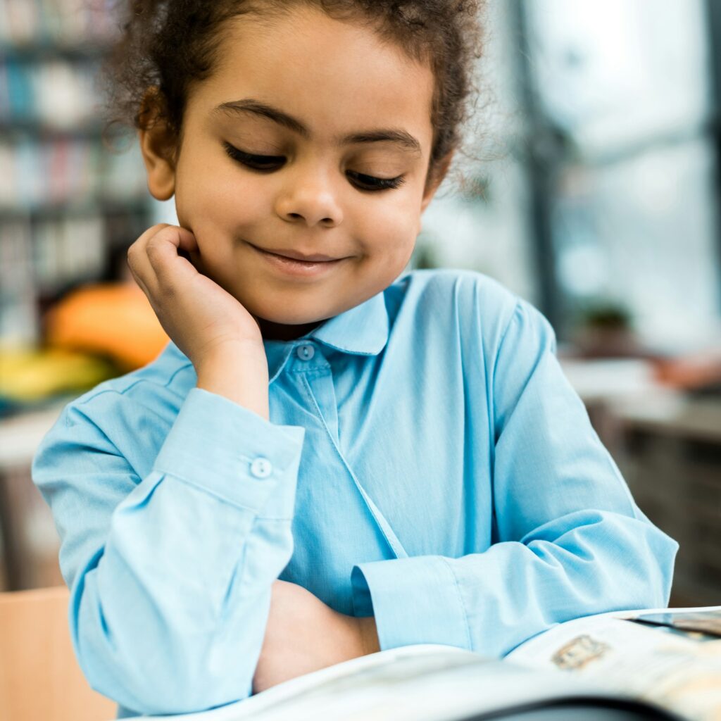 selective focus of happy african american kid smiling and reading book on table