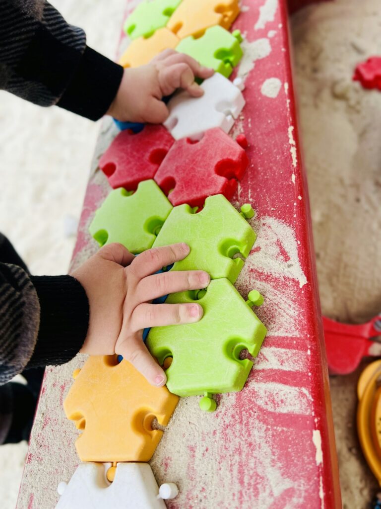 The child plays in the sandbox with colorful puzzles.